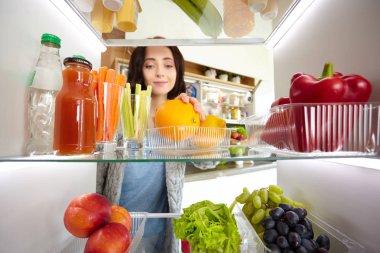 Sağlıklı yiyecek, sebze ve meyvelerle dolu açık buzdolabının yanında duran kadın portresi. Kadın portresi