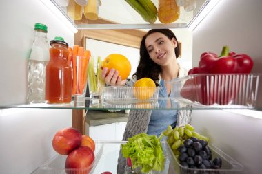 Sağlıklı yiyecek, sebze ve meyvelerle dolu açık buzdolabının yanında duran kadın portresi. Kadın portresi