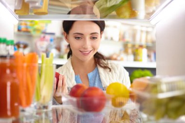 Sağlıklı yiyecek, sebze ve meyvelerle dolu açık buzdolabının yanında duran kadın portresi. Kadın portresi