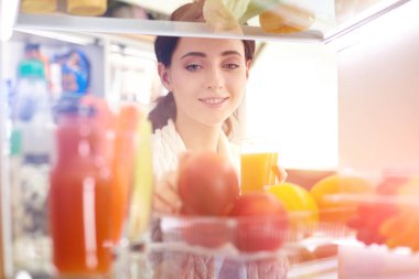 Sağlıklı yiyecek, sebze ve meyvelerle dolu açık buzdolabının yanında duran kadın portresi. Kadın portresi