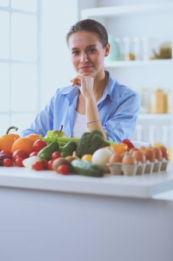 Ahşap iç kısımda meyve ve sebze dolu masada oturan genç ve tatlı bir kadın.