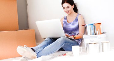 Yeni daire dizüstü bilgisayar ile oturup, boyama sırasında genç kadın portre. Dizüstü bilgisayar ile genç kadın