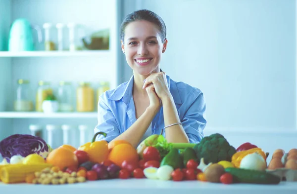 Mujer joven y linda sentada en la mesa llena de frutas y verduras en el interior de madera — Foto de Stock