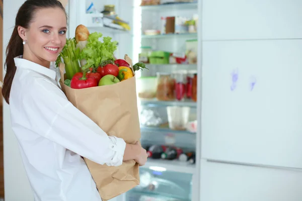 Junge Frau hält Einkaufstasche mit Gemüse in der Hand. Frau in der Küche blickt in die Kamera — Stockfoto