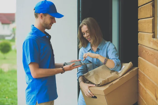 Smiling delivery man in blue uniform delivering parcel box to recipient - courier service concept. Smiling delivery man in blue uniform