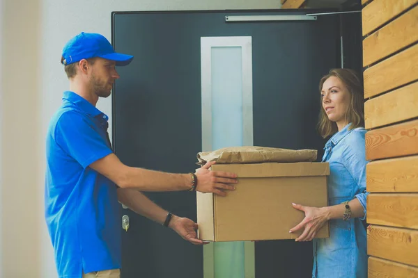 Homem de entrega sorridente em uniforme azul entregando caixa de encomendas ao destinatário conceito de serviço de correio. Sorrindo homem de entrega em uniforme azul — Fotografia de Stock