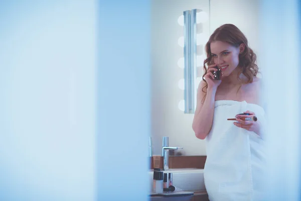 Jonge vrouw staande op badkamer met telefoon. — Stockfoto