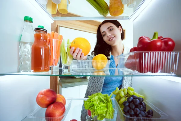 Portrait of female standing near open fridge full of healthy food, vegetables and fruits. Portrait of female — Stock Photo, Image