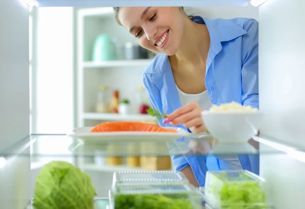 Portrait of female standing near open fridge full of healthy food, vegetables and fruits — Stock Photo, Image