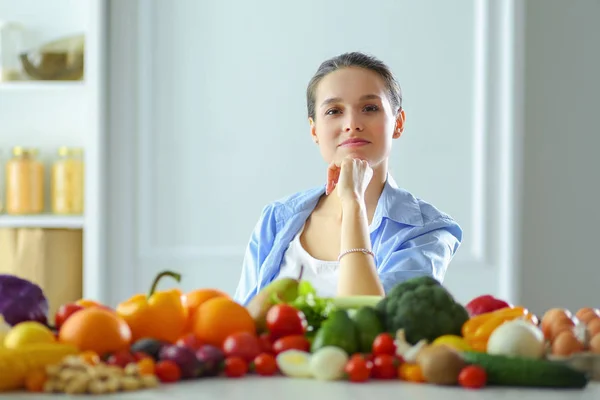 Mujer joven y linda sentada en la mesa llena de frutas y verduras en el interior de madera — Foto de Stock