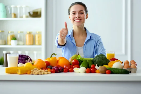 젊고 귀여운 여자 목조 인테리어에 야채와 과일의 전체 테이블에 앉아 — 스톡 사진
