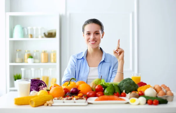 Jonge en schattige vrouw zittend aan tafel vol groenten en fruit in het houten interieur — Stockfoto