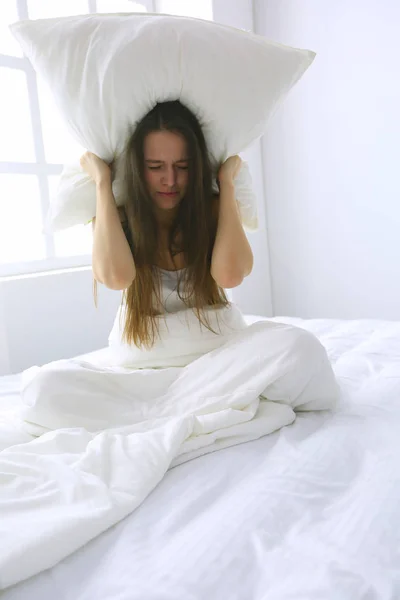 Young caucasian woman covering her head and ears with pillows — Stock Photo, Image