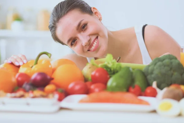 Giovane e carina donna seduta a tavola piena di frutta e verdura all'interno in legno — Foto Stock