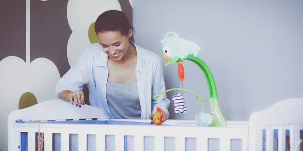 Jonge vrouw stond in de buurt van childrens kinderbed. Jonge moeder — Stockfoto