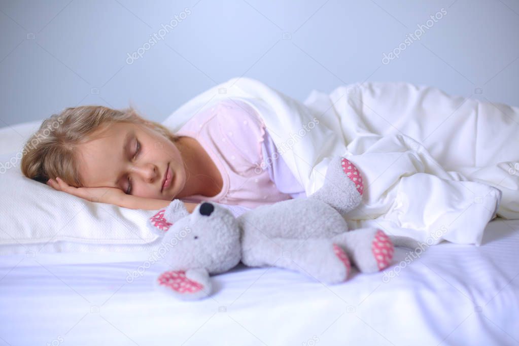 Child little girl sleeps in the bed with a toy teddy bear.