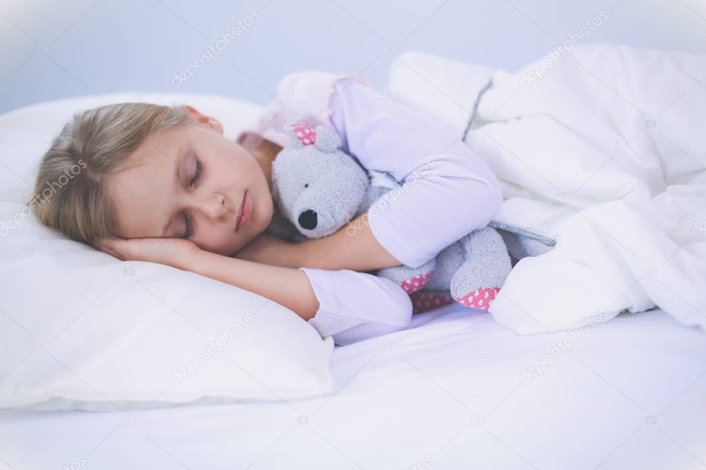 Child little girl sleeps in the bed with a toy teddy bear.