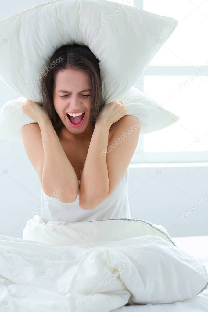 Young caucasian woman covering her head and ears with pillows