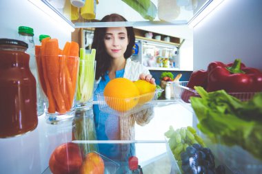 Sağlıklı yiyecek, sebze ve meyvelerle dolu açık buzdolabının yanında duran kadın portresi. Kadın portresi