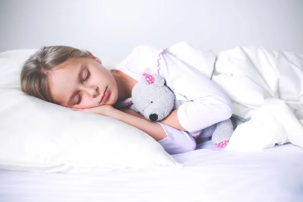 Kind meisje slaapt in het bed met een speeltje teddy beer. — Stockfoto