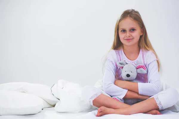 Das kleine Mädchen im Schlafzimmer sitzt auf dem Bett. kleines Mädchen trägt Schlafanzug und sitzt im Bett . — Stockfoto