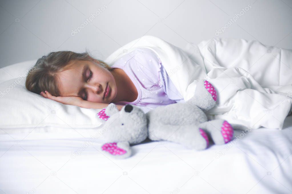 Child little girl sleeps in the bed with a toy teddy bear.