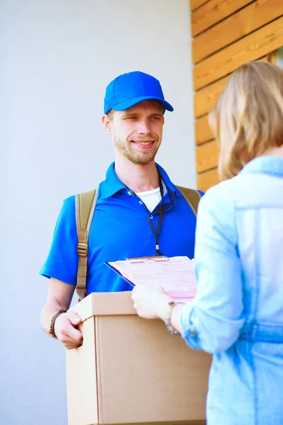 Repartidor sonriente con uniforme azul que entrega la caja de paquetes al destinatario: concepto de servicio de mensajería. Repartidor sonriente en uniforme azul — Foto de Stock