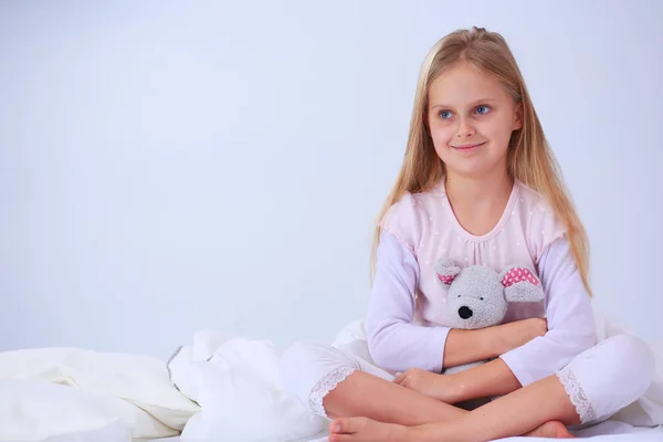 Das kleine Mädchen im Schlafzimmer sitzt auf dem Bett. kleines Mädchen trägt Schlafanzug und sitzt im Bett . — Stockfoto