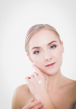 Mutlu gülümseyen genç bir kadının portresi tenine dokunuyor ya da krem sürüyor, beyaz arka planda izole edilmiş.