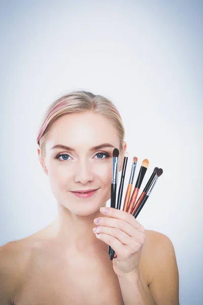 Portret van mooi jong meisje op witte achtergrond met een perfecte gezicht met veel handen met make-up borstel — Stockfoto