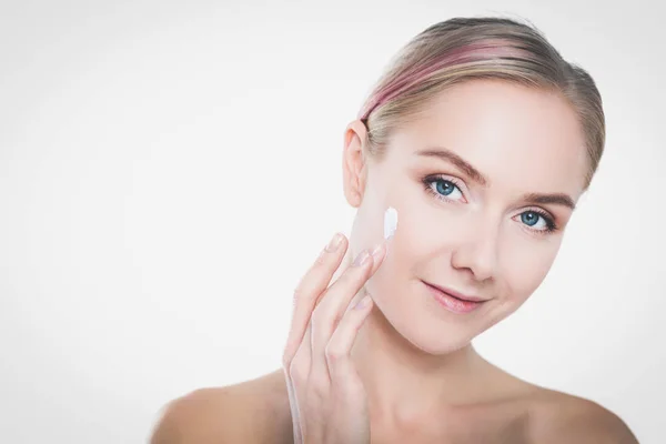 Portret van een vrolijke glimlachende mooie jonge vrouw die de huid aanraakt of crème aanbrengt, geïsoleerd over een witte achtergrond — Stockfoto