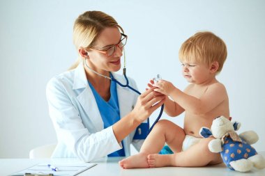 Kadın doktor, klinikte steteskoplu bir çocuğu dinliyor.