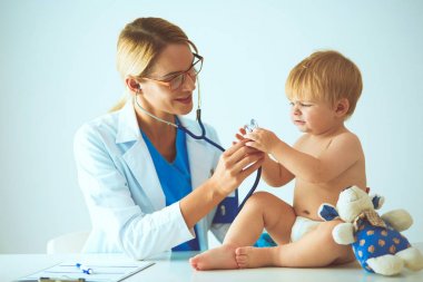 Kadın doktor, klinikte steteskoplu bir çocuğu dinliyor.