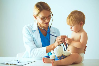 Kadın doktor, klinikte steteskoplu bir çocuğu dinliyor.