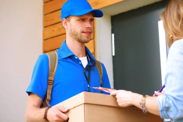 Repartidor sonriente con uniforme azul que entrega la caja de paquetes al destinatario: concepto de servicio de mensajería. Repartidor sonriente en uniforme azul — Foto de Stock