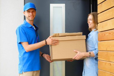 Mavi üniformalı gülümseyen kurye servis konseptine paket kutusu teslim eden teslimatçı. Mavi üniformalı gülümseyen teslimatçı.