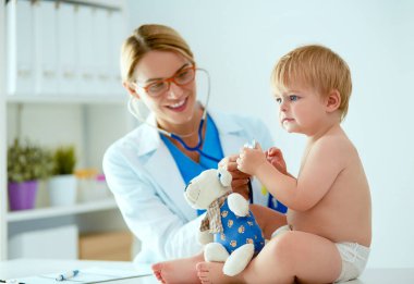 Kadın doktor, klinikte steteskoplu bir çocuğu dinliyor.