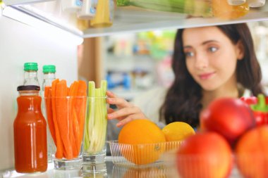 Sağlıklı yiyecek, sebze ve meyvelerle dolu açık buzdolabının yanında duran kadın portresi. Kadın portresi