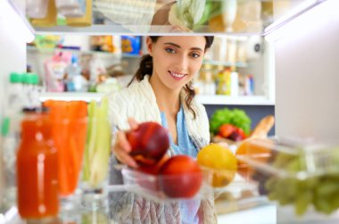 Sağlıklı yiyecek, sebze ve meyvelerle dolu açık buzdolabının yanında duran kadın portresi. Kadın portresi
