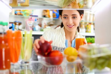 Sağlıklı yiyecek, sebze ve meyvelerle dolu açık buzdolabının yanında duran kadın portresi. Kadın portresi