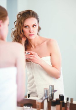 Genç bir kadın aynaya bakıyor ve makyaj yapıyor..