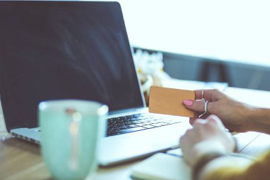 Kredi kartı tutan ve dizüstü bilgisayar kullanan genç bir kadın. Çevrimiçi alışveriş kavramı
