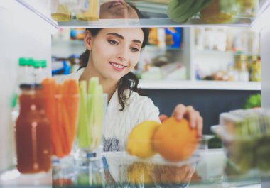 Sağlıklı yiyecek, sebze ve meyvelerle dolu açık buzdolabının yanında duran kadın portresi. Kadın portresi