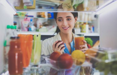 Sağlıklı yiyecek, sebze ve meyvelerle dolu açık buzdolabının yanında duran kadın portresi. Kadın portresi