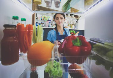 Sağlıklı yiyecek, sebze ve meyvelerle dolu açık buzdolabının yanında duran kadın portresi. Kadın portresi