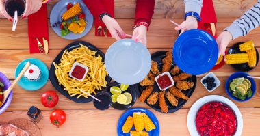 Ahşap masada otururken birlikte yemek yiyen bir grup insanın üst düzey görüntüsü. Masada yemek var. İnsanlar fast food yiyor..