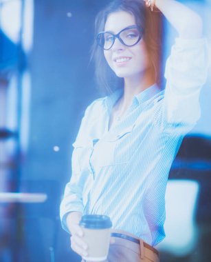 Ofis masasında dizüstü bilgisayarıyla oturan genç bir kadın. Pencereden bakıyor. Genç kadın.