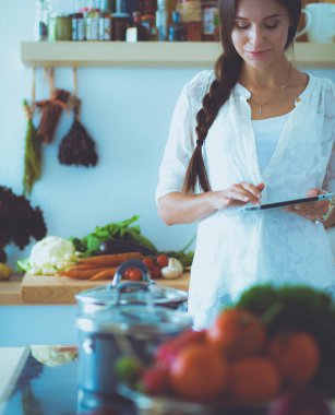 Mutfağında yemek için bir tablet bilgisayar kullanan genç kadın. Genç kadın