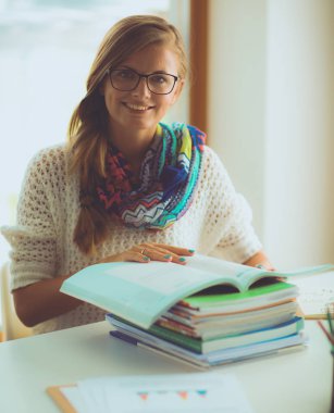 Kitapların arasında bir masada oturan genç bir kadın. Öğrenci