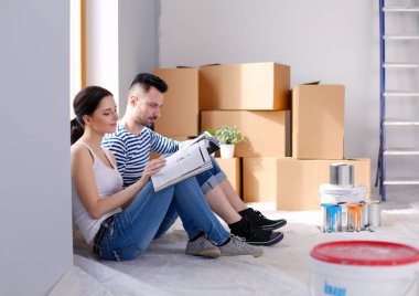 Yeni evin içini boyayan mutlu, gülümseyen genç bir çift portresi. Genç çift